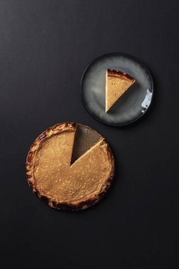 Siyah arkaplanlı ve tabakta servis edilen peynirli kek turtası. Üst manzara, düz uzanma.