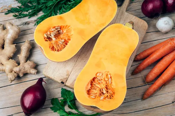 Tahta masanın üzerinde tohumlarla kesilmiş taze tereyağlı balkabağı, havuç, soğan, sarımsak, zencefil ve maydanozla çevrili. Sağlıklı vejetaryen gıda konsepti. Üst görünüm.