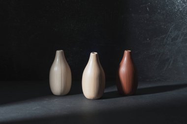 Siyah zemin üzerinde üç seramik vazo ışıkta.