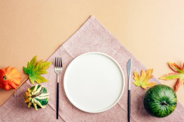 Boş tabak, çatal bıçak, balkabağı ve sarı yapraklarla sonbahar sofrası. Şükran Günü konsepti Üst manzara, düz uzanma.