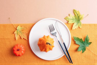 Sonbahar masa düzenleme, sarı balkabağı, beyaz tabak ve bej arka planda sonbahar yaprakları. Üst manzara, düz uzanma.