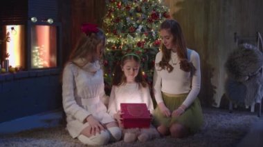 Bir hediyeyi açarken üç farklı kız ifadesi. Üç kız kardeş oturma odasında Noel ağacının yanında oturur ve hediyeleri açarlar. Tatil için dekore edilmiş oturma odası olan bir ev.
