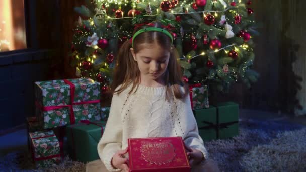 豪華な装飾が施された部屋にクリスマスツリーのそばに立つ女の子と彼女の特別な贈り物を開く 歌う光の胸 クリスマスのコンセプト4Kクローズアップ映像 — ストック動画