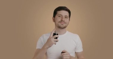 Neşeli adam boynuna şehvetli ve pahalı bir parfüm sıkmış. Güzellik, parfüm ve bakım kavramı. Parfüm şişesi tutan ve spreyleyen mutlu genç adamın portresi.
