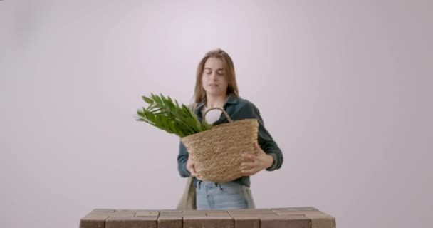 お店から戻ってきた若い女性は 部屋の花のあるコットンと肩にエコバッグで作られた編んだバッグで戻ってきました 緑の花を植え替えたい主婦 — ストック動画