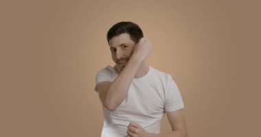 Beyaz tişörtlü, taraklı saçlarını tarayan, banyo aynasına bakan kendinden emin ve çekici bir yetişkin. Yakışıklı, gülümseyen sakallı adam sabah saçını yapıyor. Erkeklerin saç bakım konsepti.