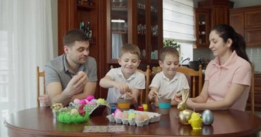 a happy family sits at a table and paints Easter eggs. the boy gives five to his mother