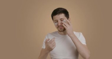 Man in a good mood and applies moisturizing eye patches after the morning,evening routine. A brunette man with a beard smiles at the camera and waits for the patches to take effect, closing his eyes.