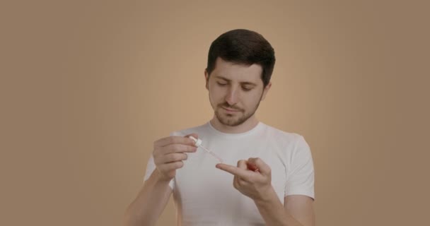 一个英俊的年轻人 手指上戴着长笛 在镜头前微笑 用营养血清喂人 男人在浴室镜子前做皮肤护理 男子个人卫生概念 — 图库视频影像