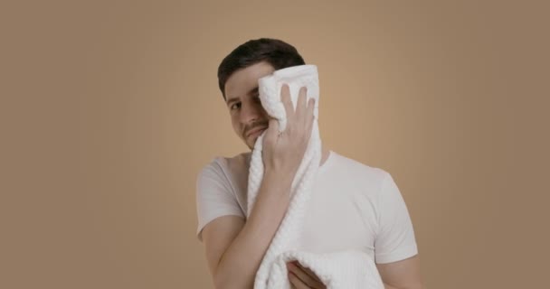 一个年轻英俊的男人穿着一件白色的T恤 洗脸或刮胡子后用柔软的毛巾擦拭脸 在浴室享受他早上的日常生活 这反映了他的镜像 常规概念 — 图库视频影像