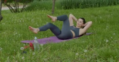 active sportswoman doing her morning training in the park. Lie on your back, with your hands behind your head, and raise your hind limbs a little and move them at the same time.