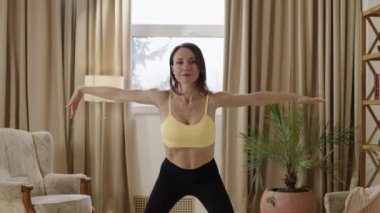 Young yoga, fitness, stretching trainer filming online class. Woman with very toned and muscular slim body doing exercises in a bright sunny and luxurious room. Healthy lifestyle concept