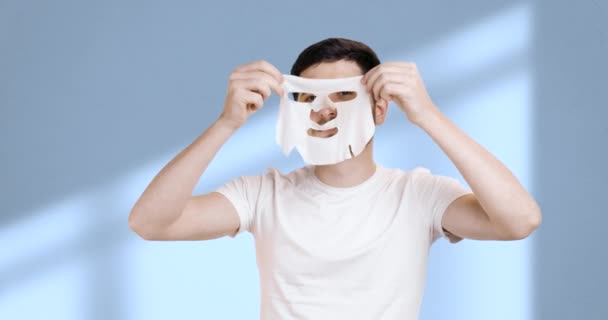一个男人从他的脸上摘下他的白箔面具 微笑着的画像 脸干净完美的男人在浴室里做整容 化妆品程序的概念 — 图库视频影像