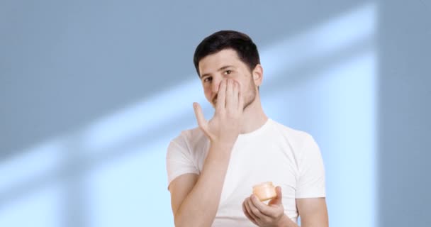 Jovem Atraente Camiseta Branca Aplicando Hidratante Seu Rosto Enquanto Olha — Vídeo de Stock