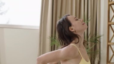 Atletik vücudu olan bir kadın diz çökmüş, sakin ve gözleri kapalı meditasyon yapıyor. Mavi spor takım elbiseli güzel bir kadın stresi azaltmak ve vücut esnekliğini geliştirmek için yoga ve esneme egzersizleri yapıyor..