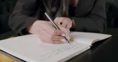 İş kadını elle yazıyor ya da kağıt planlamacılığında yapılacaklar listesi hazırlıyor ve işleri yönetiyor. Bir kadının tüm görevlerini bir çalışma kitabına yazarken ve planlarken yakın plan görüntüsü.