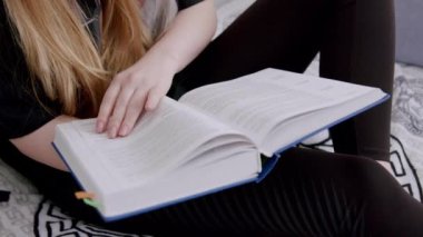Uzun sarı saçlı kız yatakta oturuyor ve kalın bir kitap okuyor. Yaz kampındaki kız okul konulu bir kitap okuyor. Genç bir kadın yavaşça sayfaları çeviriyor. Okuma hobisi
