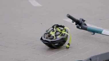 Elektrikli scooter ve lüks bir beyaz arabanın yol kazasından sonra asfaltta dönen koruyucu başlıklı kaskın yakın çekimi. Yol kazaları kavramı