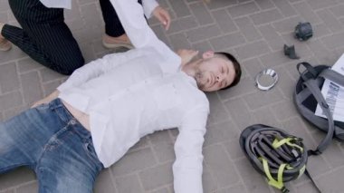 Trafik kazasından sonra asfaltta yatan bir adamın yakın plan görüntüsü. Sürücü, adamın sağ olup olmadığına bakmak için hızla ona doğru koşar ve göğsüne bastırarak ilk yardım uygular.