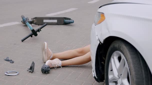 交通事故の後 白い高級車が電動スクーターに乗っていた少女を襲い アスファルトに落ちました 損傷した車の前には 地面に横たわっている傷ついた人の足を見ることができます — ストック動画