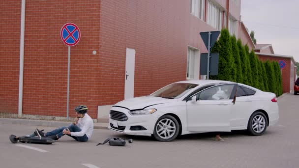车祸后 司机立即停车 向躺在沥青路面上的男子跑去 对他进行急救 一辆白色轿车和一辆电动车的交通事故 危险的交叉口 — 图库视频影像