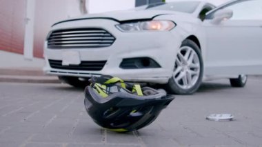 Elektrikli scooter ve lüks bir beyaz arabanın yol kazasından sonra asfaltta dönen bir kaskın yakın plan çekimi. Yol kazaları kavramı