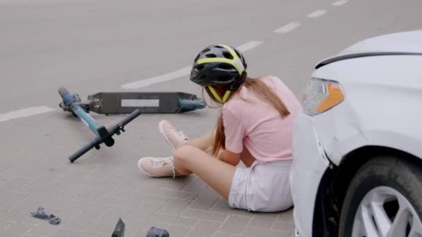 年轻女人头上戴着防护头盔 坐在沥青路面上 膝盖疼痛 车祸后擦伤腿 那个骑自行车的人在等救护车 — 图库视频影像
