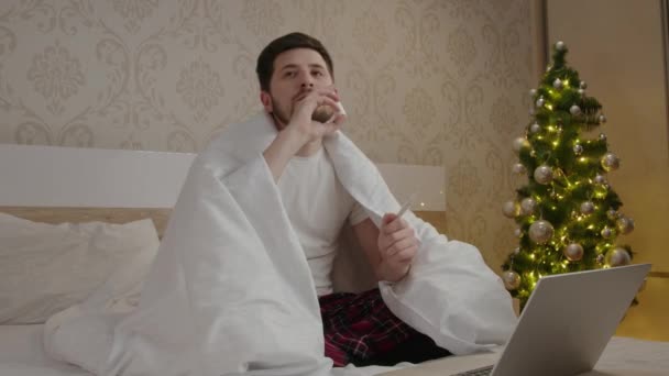 在家里穿着睡衣的忧郁而冷酷的男人在他的鼻子上喷出火花 发烧的病童被包裹起来 在电脑上看电影 并在平静的气氛中庆祝家中的寒假 — 图库视频影像