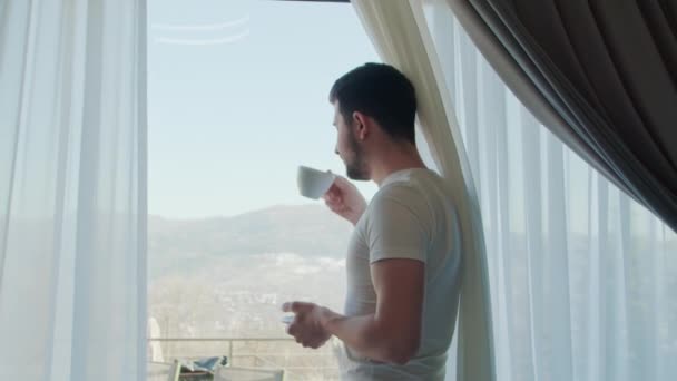 在宁静的卧室里 男人喝着咖啡 透过全景窗户凝视着 静默的片刻沉思加深了他的沉思宁静的场景 外面的镜子滋长着沉思宁静的心情 — 图库视频影像