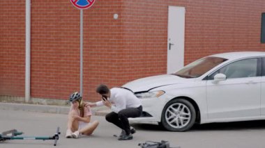 Scooter ve araba kazası geçiren şoför, yaralı kadın sürücüye yol güvenliği konusunda yardım ediyor. Scooter kazası sahnesi, scooter kazalarından sonra yardım ve çabuk iyileşmenin öneminin altını çiziyor