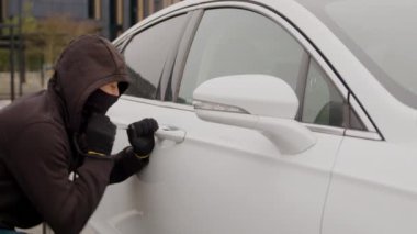 Siyah kapüşonlu bir hırsız beyaz bir araba kapısının kilidini zorla açmak için tornavida kullanıyor. Araba hırsızlığı gibi gözüpek bir hareket sergiliyor. Araba hırsızlığı.