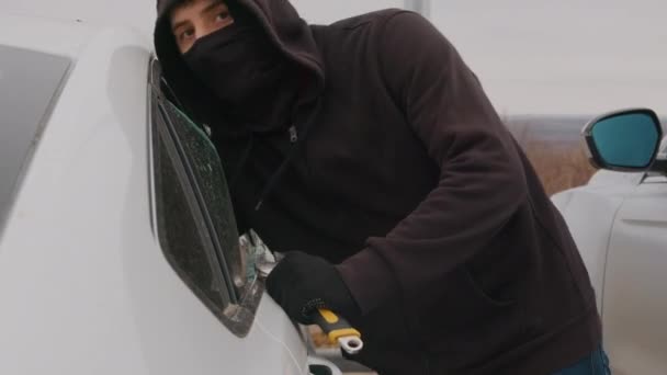 マスクの後ろに隠されたフード付き泥棒は 車の散らばった窓を介してステルシーに財布を積み重ねます — ストック動画