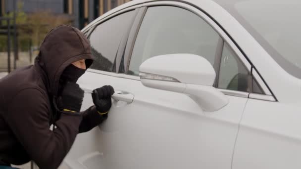 一名身穿黑色帽衫的小偷用螺丝刀强行撬开了一辆白色汽车车门的锁 展示了一起盗车的大胆行为 汽车盗窃 — 图库视频影像