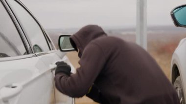 Araba hırsızı, araba hırsızlığını gösteren bu görüntüde tornavida kullanarak zorla beyaz bir arabanın kilidini açmış.