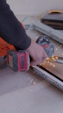 Adamın metali dairesel öğütücüyle kestiği dikey video. Atölye havadaki kıvılcımları keserken makinelerin uğultusuyla yankılanır. Görevin yoğunluğunu vurgulayan metali öğütücüyle keser.