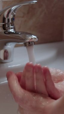 Bir insan suyun altında ellerini yıkayarak kişisel hijyen pratiği yapar. Dikey videoyu kapat. Kişisel hijyen, zararlı bakterilerin el yıkamasının engellenmesine yardımcı olur.