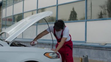 Otomobil servis garajında, tamirci antifriz dolduran açık kaputlu araca bakar otomobillerin düzgün çalışmasını sağlamada otomobil hizmet merkezlerinin önemini vurgular