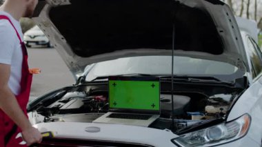 Otomobil teknisyeni yeşil ekran kromatonlu dizüstü bilgisayar kullanarak arabaya teşhis koyuyor. Otomotiv tamiri için kullanılan kromaanahtar teknolojisi modern yaklaşım, bozuk araçları teşhis etmenin öneminin altını çiziyor