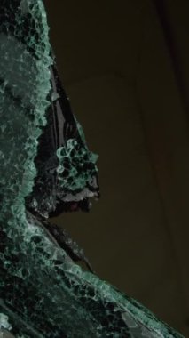 Kırık cam araba penceresi dikey görüntüsü. Kırık parça hırsızı arkasında elle tutulur kanıtlar bırakıyor. Olay yeri, suç unsurlarına karşı savunmasız araçlar sunuyor.