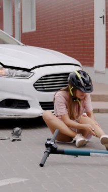 Araba ve elektrikli scooter çarpışması, kadın sürücünün bacağını dikey çekimde tuttuğunu gösteriyor. Araba ve elektrikli scooter kazası geçiren kadın sürücü yaralı bacağını tutarak acı içinde kıvranıyor