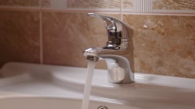 Lavabonun altındaki musluktan gelen temiz su akıntısı porselen lavabonun altında. Metalik çelik musluk, temiz su, temiz su, temiz banyo, hijyenik temiz su, musluktan dökülüyor.