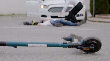 Elektrikli scooter kazası sonrası arka planda kaza sonucu yaralanan biri var. Yol güvenliği kazaları çarpışma sonrası araba elektrikli scooter kazaları trafik kazaları