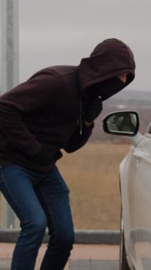 Gölgeli figürlü kapüşonlu ceket dikey video çalmak için park etmiş arabayı gizlice kırmaya çalışıyor. Yaygın araba hırsızlığı kentsel alanlarda endişe uyandıran araç güvenliği araba hırsızlığı suç faaliyetlerini çaldı