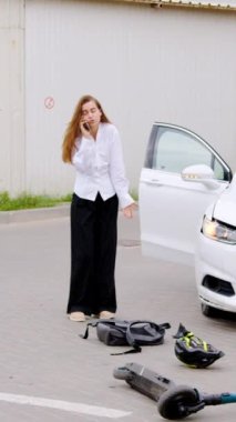 Elektrikli scooterın hasarlı scooter 'ı çarptıktan sonra kadın sürücünün telefonda konuştuğu kaza sonrası yer yatar. Trafik kazası, araba, elektrikli scooter, kadın sürücü, telefon.