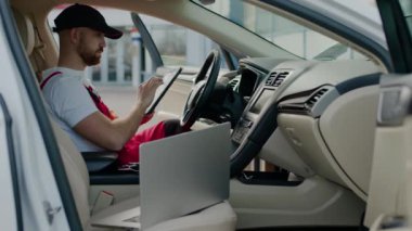 Araba dizüstü bilgisayarında oturan otomotiv teknisyeni tanısal test araçları otomobil servisi arızası yapıyor. Araç ustası mekanik dizüstü bilgisayardan faydalanıyor arabaların sorunlu otomobil servis merkezlerini teşhis ediyor