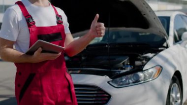 Tamir edilmiş arabanın yanında duran otomotiv mühendisi başarılı bir tamirat olduğunu gösteriyor. Otomobil hizmet merkezi mühendisi başarılı araba tamiri uzmanlığı verdi