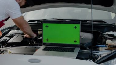 Usta tamirci, kaput altında araba tamiri yapmak için yeşil renkli ekranlı dizüstü bilgisayar kullanır. Usta tamirci otomobil servisi, dizüstü bilgisayarı yeşil renkli ekran onarım teknolojisi ile çalışır.