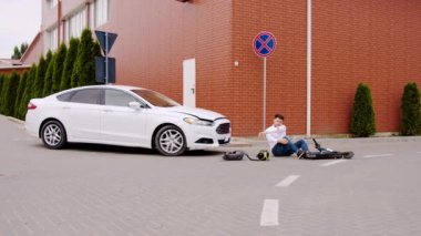 Elektrikli scooter 'a çarptıktan sonra yaralanan erkek scooter sürücüsü, araba kazasından sonra yerde yatıyor. Otomobil kazası. Elektrikli scooter, yerde yaralı erkek scooter sürücüsü.