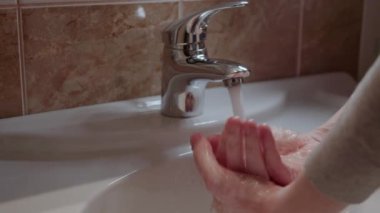 Adam ellerini temiz suyla yıkıyor. Adam suyu açar ve dışarı çıktıktan sonra ellerini iyice temizler. Büyük ve temiz ortak banyo. Bakterilerin yayılmasını önlüyor