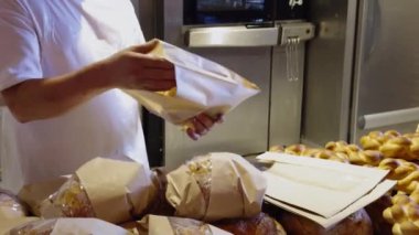 Hamur ürünlerini bir pastanede paketleme süreci. Fırıncı ekmeği fırından yeni çıkmış bir şekilde eko kağıt torbalarda paketliyor. Başarılı bir fırın işinin çalışma süreci